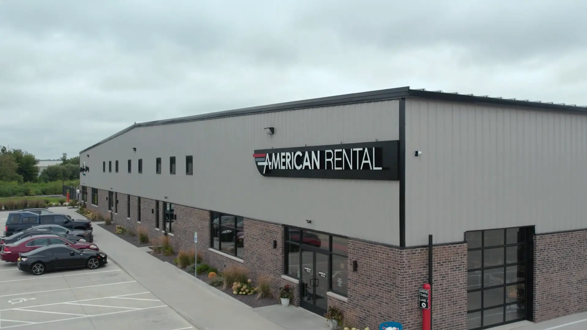 The front of American Rental's building in Morton, IL. Cars are parked outside the front and the first drive-thru sign is visible at the bottom.